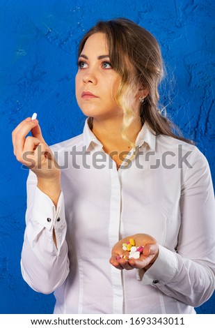 Young woman on a blue background take pills. Portrait of a serious woman with drugs in her hands