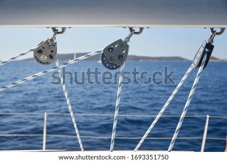 Close-up view of sailboat ropes at sunny weather, pulleys and ropes on the mast, Yachting sport, ship equipment, sea is on background Royalty-Free Stock Photo #1693351750