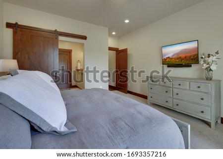 Beautiful large luxury new bedroom with great design, beige, grey and white tones, TV dresser, rich wooden doors, window blinds and grey carpet.  Expensive furniture. Doors open to 