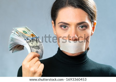 a young woman with a closed adhesive tape in her mouth holds a large amount of cash in her hand. concept of bribery of a witness, corruption, bribery. Royalty-Free Stock Photo #1693360453