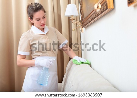 A uniformed maid is holding furniture cleaning spray. Cleaning of the hotel room. Copy space.