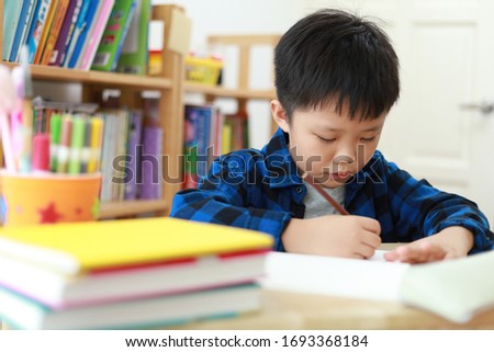Portrait of smart little Asian boy sitting at desk and doing school work. Education concept.