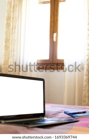 Vertical photography of a laptop in bed while remote working from home and a bright window in the background. Template for advertising.