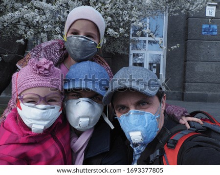 young family in respirators during quarantine in a city park against the background of a blossoming tree

