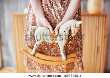 Baby rocking horse in hands behind her back