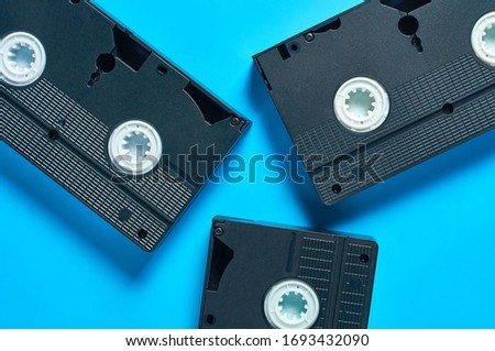 Scattered black old plastic vhs video cassettes lies on blue desk. Concept of 90s. Top view. Close-up