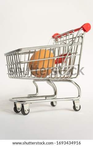 toy little consumer food trolley from steel with red plastic handle on a gray background with one fresh egg inside. empty space, close-up