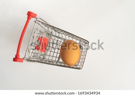 toy little consumer food trolley from steel with red plastic handle on a gray background with one fresh egg inside. empty space, top view