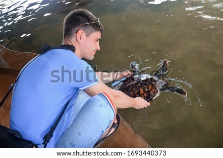 Young brunette guy with camera releases turtle, volunteer saves turtles, animal protection, boy takes pictures of turtle. saving animals in Sea Turtles Conservation Research Project  Center in Bentota