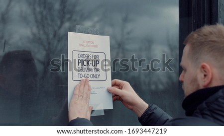 Caucasian male puts a Temporary closed due COVID-19 pandemic sign on a window. Coronavirus small business shutdown Royalty-Free Stock Photo #1693447219