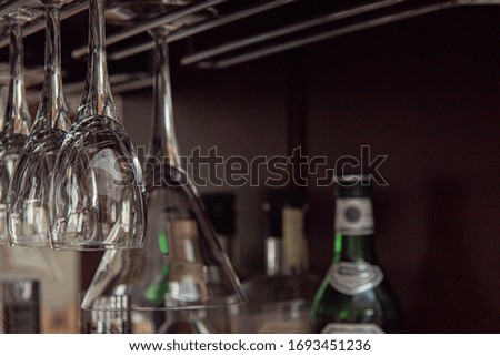 clear glass upside down martini and wine glasses inside a bar with liquor bottles in background
