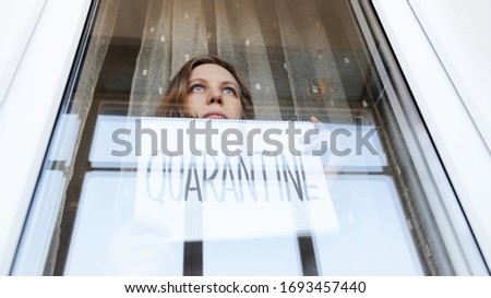 Woman looking through the window and holding a handwritten sign saying "Quarantine".