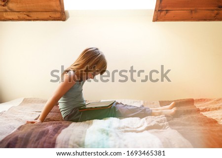 toddler girl sitting bed on the looking at tablet on her legs
