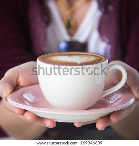 woman giving a hot cup of coffee, with heart shaped froth art