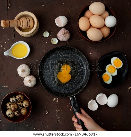 top view of woman hand frying egg with butter  garlic  eggs around on maroon background