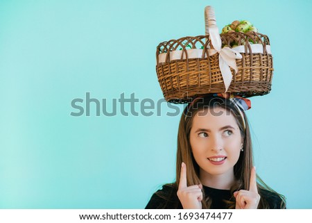 young beautiful girl holding an Easter basket on her head and smiling on a blue background. Tradition of Easter. Religion symbol. Basket with eggs. Eggs hunt. Happy Easter.