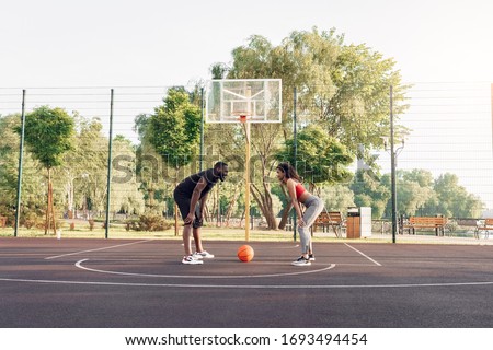 Young african descent couple standing on centercourt outdoors ready to start basketball game looking at each other smiling cheerful