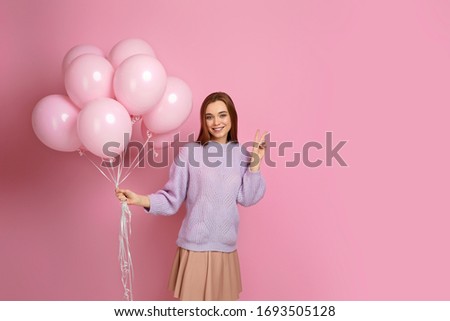 beautiful smiling caucasian girl with pastel pink air balloons showing peace gesture isolated over pink background. happy young woman on a birthday holiday. space for text