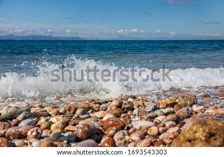 Spring beautiful day by the sea with waves on the pebbles beach and clean blue sky in South Athens, Greece.