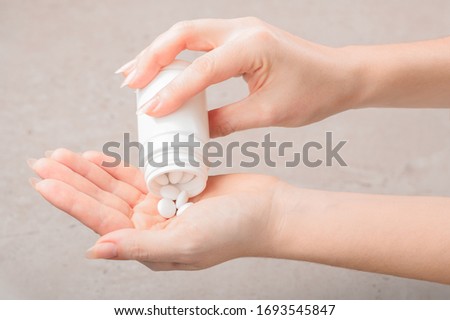 The girl pours a white tablet or vitamins or food Supplement into her hand from a white bottle. Concept of treatment, prevention or diet.
