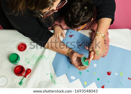 special education teacher and student in a gown are painting with their hands a birthday wreath and a yellow cardboard with acrylic paints on the table. plastic craft therapy.