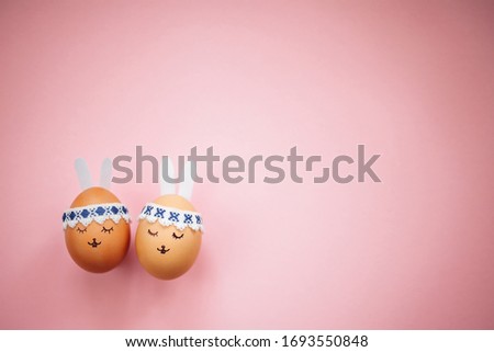 Two little easter eggs with a painted drawn rabbit faces and ears on them in laying on the pink table isolated. Easter holidays decorations, preparations concept. Holy religious day. Copyspace