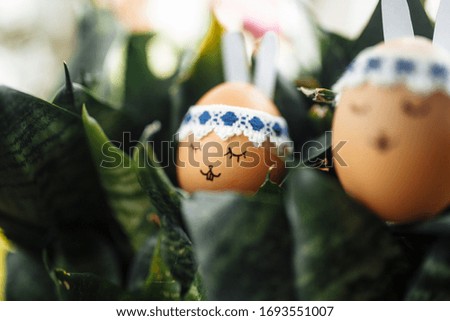 Two little easter eggs with a painted drawn rabbit faces and ears on it laying in the green flower bushes. Easter holidays decorations and preparations concept. Holy religious day