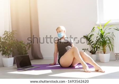 alone girl in medical mask doing yoga exercises on the floor in the light room during quarantine of covid 19 cotonavirus stay home safe world.
