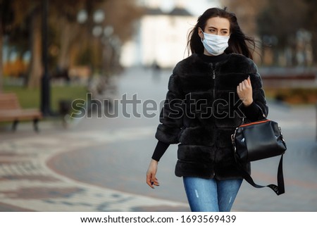 A masked girl is walking along the street. Coronavirus infection (COVID-19) Royalty-Free Stock Photo #1693569439