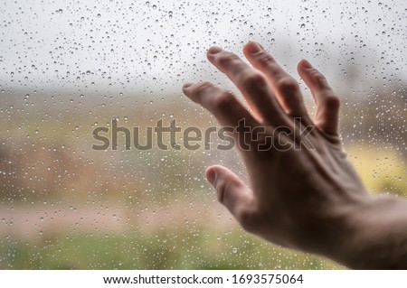 Man touches rain-soaked window pane as a symbol of wanderlust and longing Royalty-Free Stock Photo #1693575064