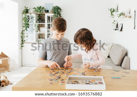 Brother and sister playing puzzles at home. Children connecting jigsaw puzzle pieces in a living room table. Kids assembling a jigsaw puzzle. Fun family leisure. Stay at home activity for kids. Royalty-Free Stock Photo #1693576882