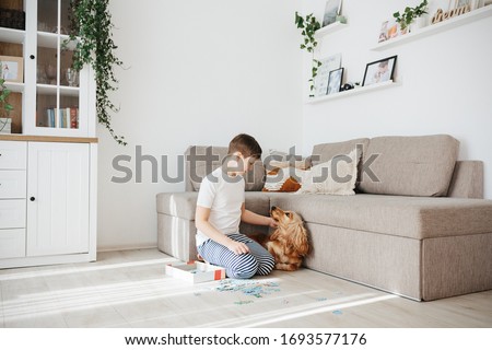 10 years boy playing puzzles at home. Child connecting jigsaw puzzle pieces sitting at floor in a living room. Playing with dog. Fun family leisure. Stay at home activity for kids.