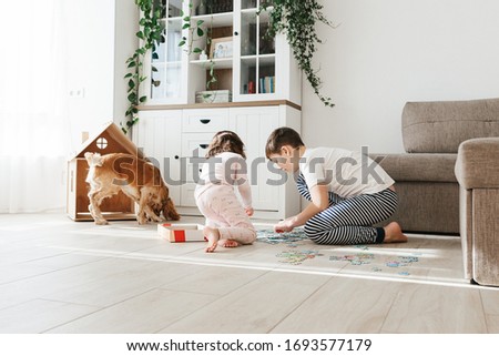 Brother and sister playing puzzles at home. Children connecting jigsaw puzzle pieces in a living room table. Stay at home activity for kids.