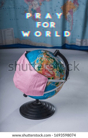 Globe in a medical mask on the background of a blurred world map with the inscription Pray for world.