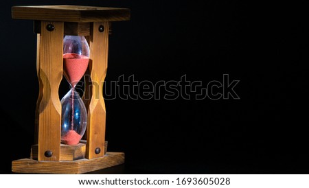 an old wooden hourglass with pink flowing sand in the left part of the frame. the lower part is filling