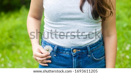 Moody picture of a dandelion flower in a jeans pocket on green background. Young woman in the summer field.