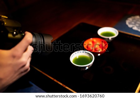 Photographing traditional japanese cups with matcha green tea bowls and strawberries in house with black lacquered wood table and dessert dish background