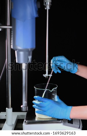 The hands of the cosmetologist in gloves mix the ingredients for making the cream. Photo on a black background. Copy space.