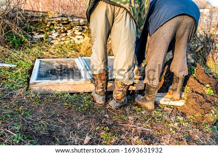 Two people, father and son, men working on vegetable winter garden for raised bed cold frame in Ukraine dacha Royalty-Free Stock Photo #1693631932