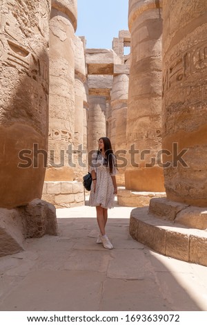 Young beautiful woman taking pictures between the columns of the hypostyle hall of Karnak's temple in Luxor, Egypt. Travel and vacation concept