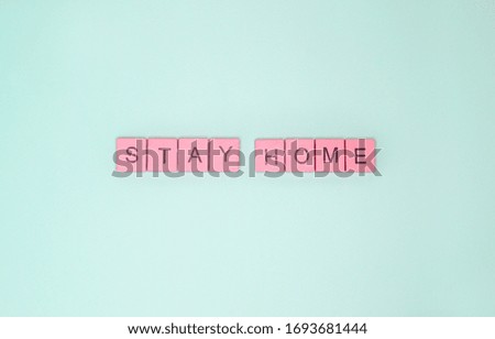 Words "stay home" made of pink wooden letters on light turquoise background