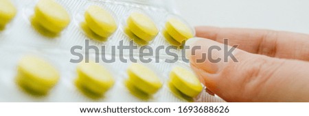 Blister with yellow vitamins in female fingers closeup