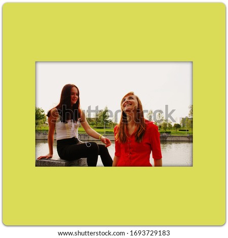Photo in a frame with the image of two laughing girls in a park on a light yellow background
