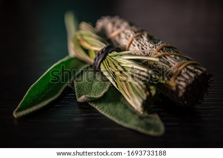 Closeup of Fresh & Dried Sage Native American Smudging Wiccan Bundles With Braided Sweet Grass Herbs On A Black Wooden Table Surface