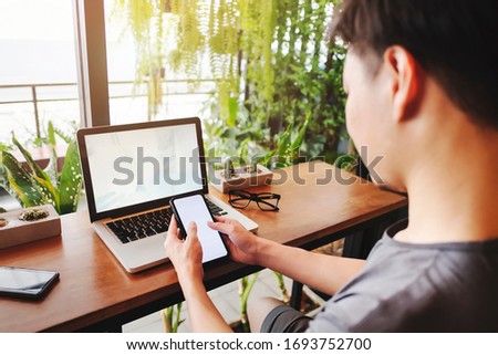 Man using mobile smart phone and notebook./Mockup image computer,cell phone blank screen for hand typing text,Work at home.