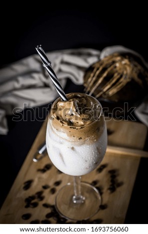 
Dalgona coffee in glass cup with beans on wooden black background
