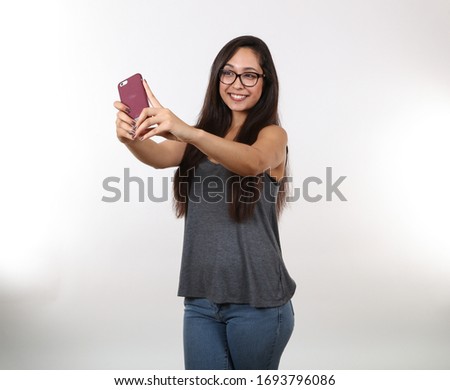 A young pretty female wearing glasses takes a selfie with her cell phone.