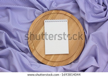 notebook with blank cover and circular cutting Board on a purple striped tablecloth, top view. space for editing your text or image. mockup, template, and layout.