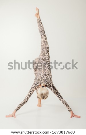 Studio shot of a young fit blonde woman doing yoga exercises in leopard or panther printed dress.