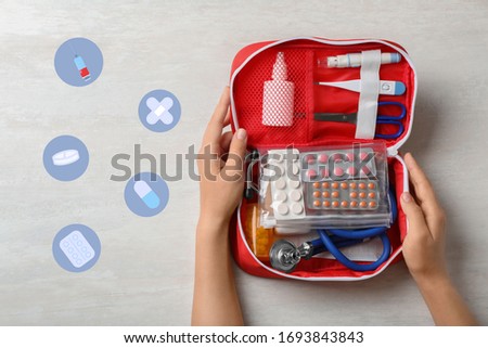 Woman holding first aid kit on white wooden table, top view
